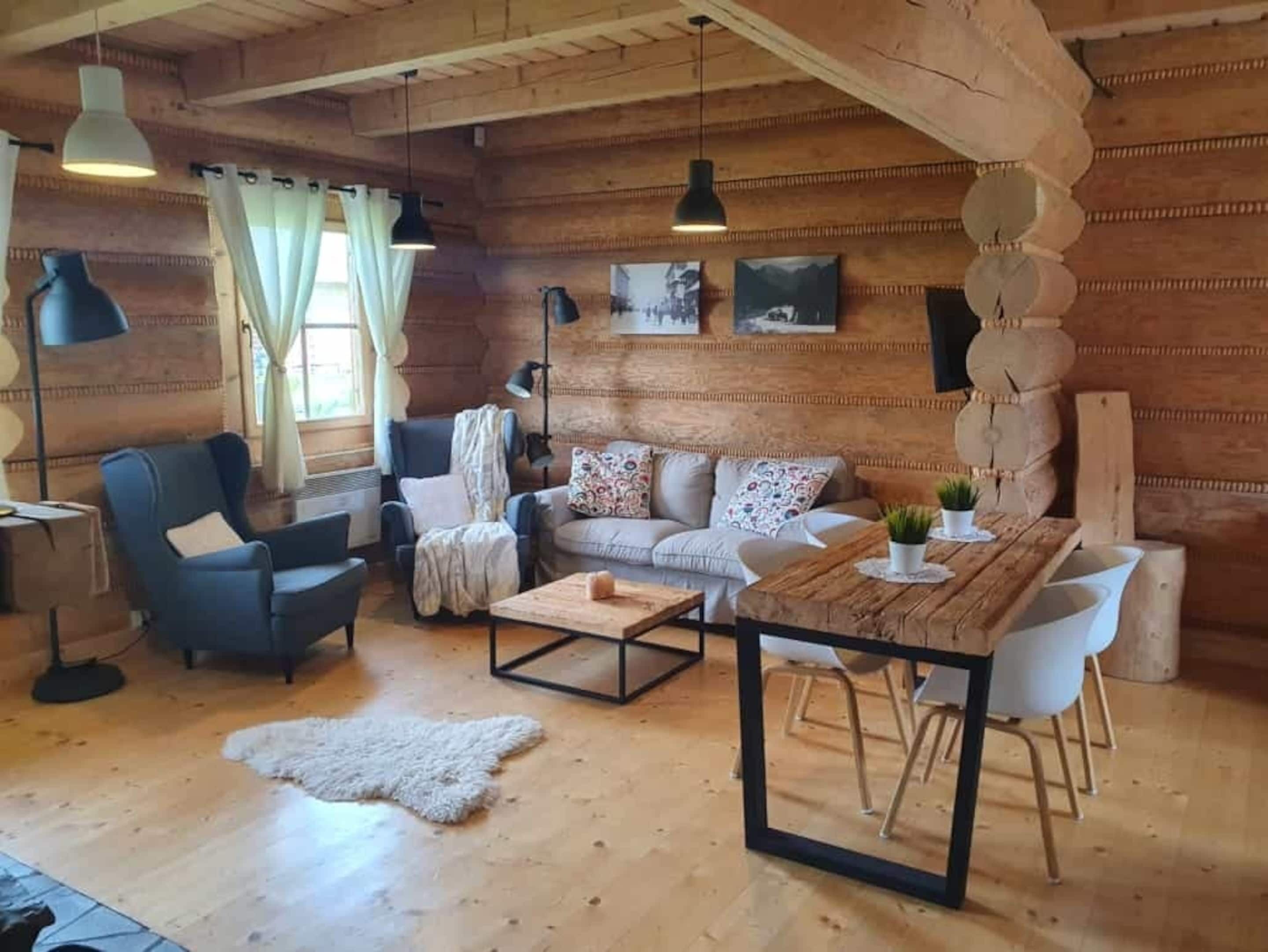 Ein gemütliches Blockhaus-Interieur mit Holzboden, einer Couch, einem Sessel, einem Couchtisch und Pendelleuchten.
