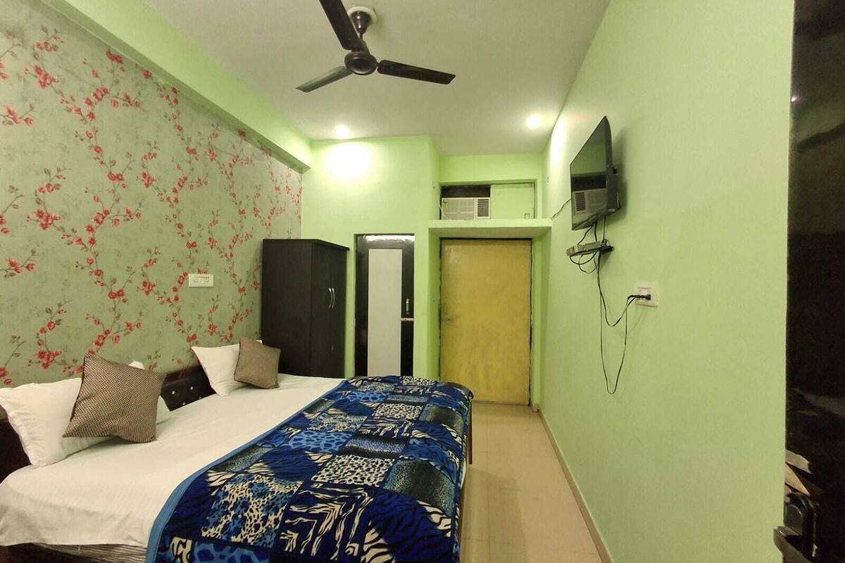 A bedroom with a bed, a ceiling fan, a wardrobe, a television, and an air conditioning unit.