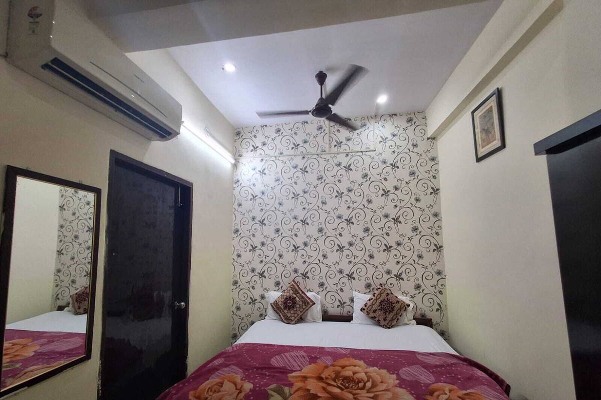 A bedroom with a bed, a ceiling fan, patterned wallpaper, and a mirror.