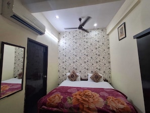 A bedroom with a bed, a ceiling fan, patterned wallpaper, and a mirror. - Inn Royal by Lakhraw Rd Varanasi (Nasirpur)