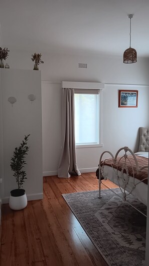 Ein Schlafzimmer mit Bett, einem Fenster mit Vorhängen, einem Heizkörper, einer Topfpflanze und einem Teppich.