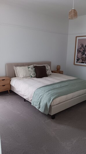 Ein Schlafzimmer mit einem Bett, einem Nachttisch, einer Lampe und einem gerahmten Bild an der Wand.
