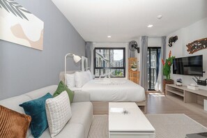 Una habitación de hotel moderna con sofá, cama, televisor y un ventanal grande.