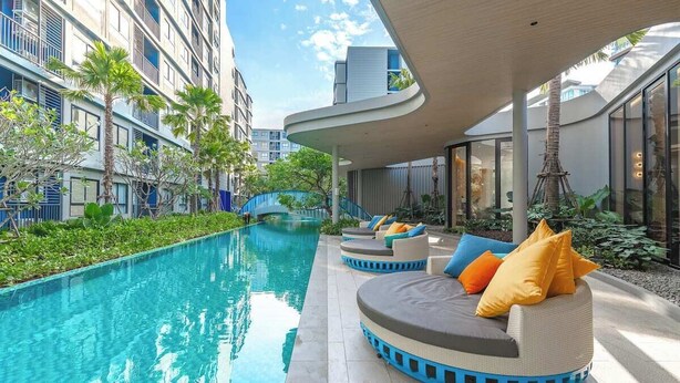 A poolside area with a curved seating arrangement, a clear pool, and modern buildings in the background. - Modern Condo with Pool View D Condo Phuket C175 (ตำบล กะทู้)