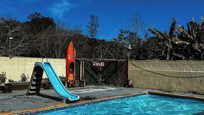 A swimming pool with a slide, a red speaker, and a sign that reads 'Hawaii Dera.' - Camping Mairiporã (Mairiporã)