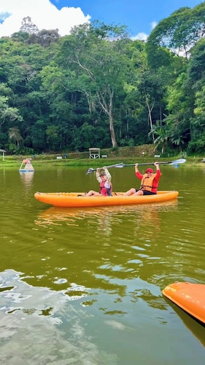 Two people kayaking on a calm river surrounded by dense greenery. - Camping Mairiporã (Mairiporã)