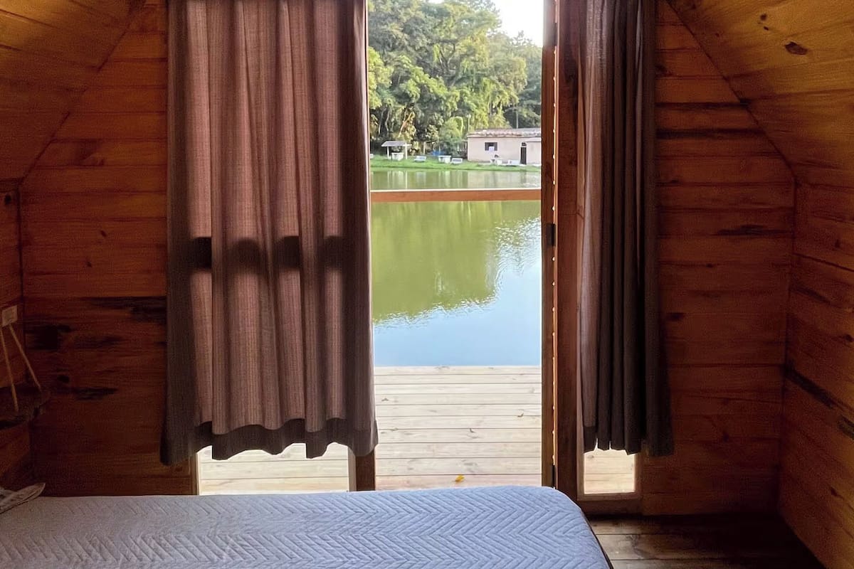 Ein Zimmer mit einem Bett, Holzwänden, einem Fenster und Blick auf einen See.