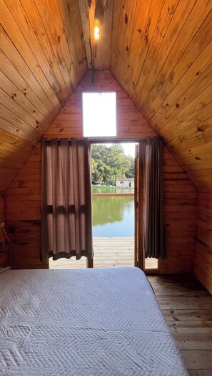 Une pièce avec un lit, des murs en bois, une fenêtre et une vue sur un lac.