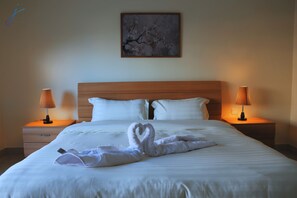 A hotel room with a neatly made bed, two bedside lamps, a wooden headboard, and a framed picture on the wall.