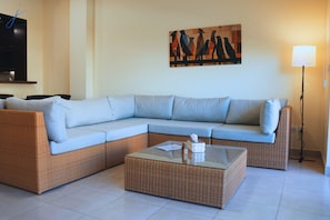 A living room with a sectional sofa, a glass coffee table, a painting on the wall, and a floor lamp.