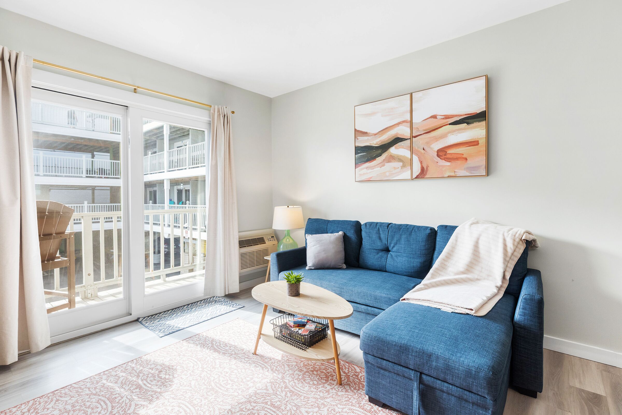 A modern living room with a blue sofa, a small round coffee table, a potted plant, and a view of a balcony with a railing.