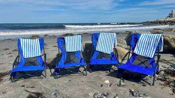 Four beach chairs with blue and white striped towels, arranged on a rocky beach with the ocean in the background.
