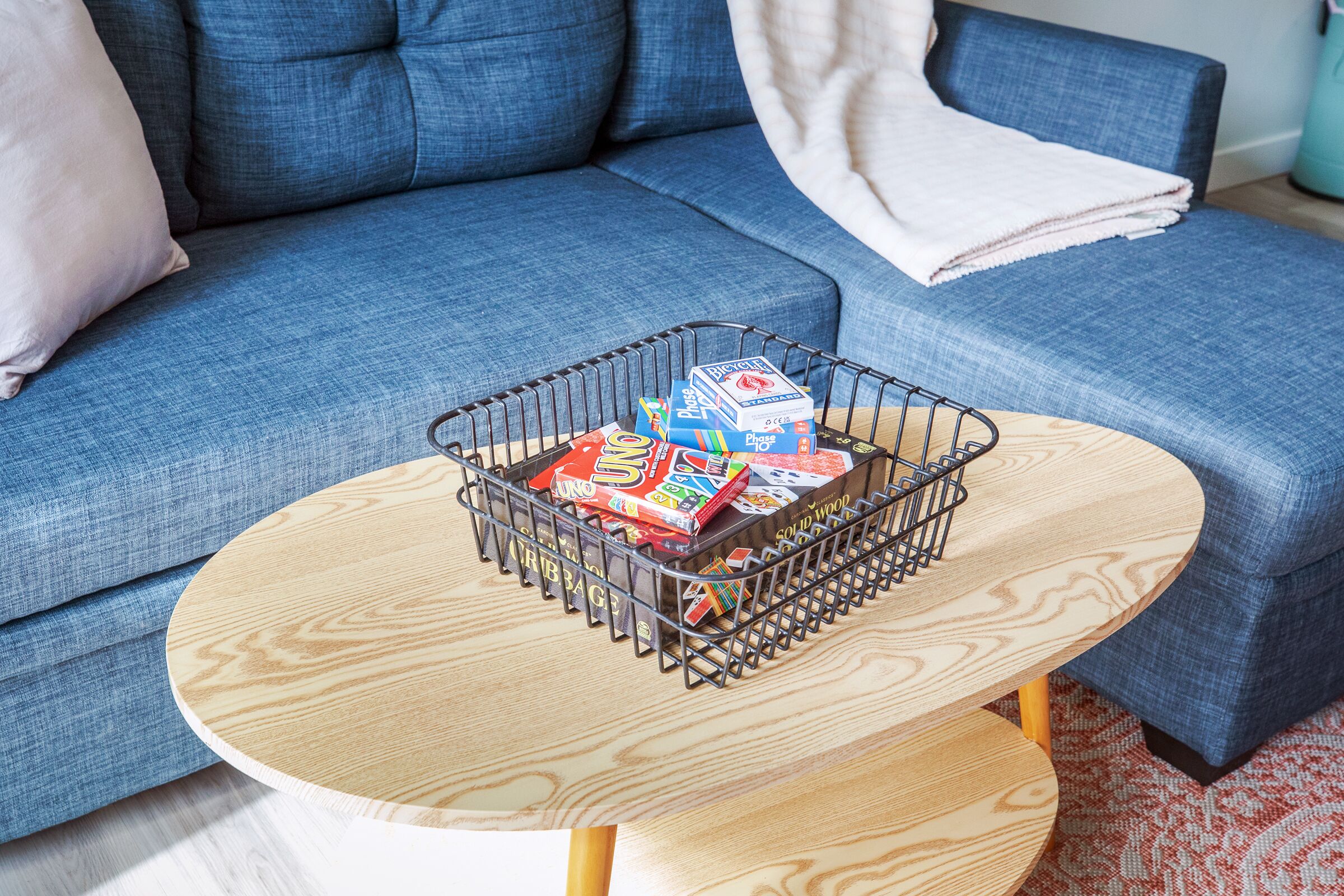 A living room with a blue sofa, a wooden coffee table, and a metal basket containing board games.