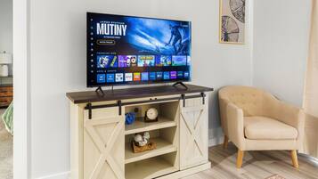 A flat-screen TV mounted on a wooden entertainment center with a sliding barn door, a beige armchair, and a patterned rug on a wooden floor.