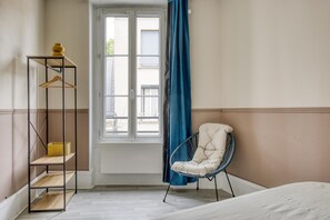 Ein Zimmer mit einem Bett, einem Sessel, einem Kleiderschrank und einem fenster mit Vorhängen.
