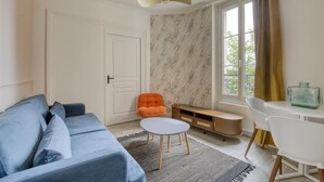 A modern living room with a blue sofa, an orange chair, a small white table, and a marble-patterned wall. - Lola Homes " Contemporary and warm apartment " (Puteaux)