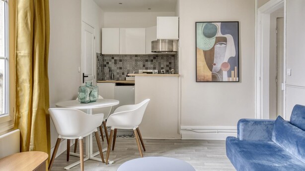 A modern living room with a blue sofa, a dining area with white chairs, and a kitchen with patterned backsplash. - Lola Homes " Contemporary and warm apartment " (Puteaux)
