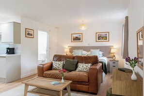 Ein modernes Hotelzimmer mit Ledersofa, Holztisch, Bett mit Kopfteil, Nachttischlampen, einem kleinen Nachttisch und einem Spiegel.