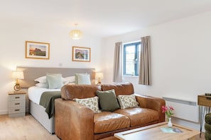 A bedroom with a bed, a leather sofa, a bedside table, a lamp, a picture frame, and a window with curtains.