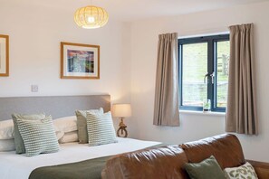 A hotel room with a bed, a window with curtains, a lamp, and a framed picture on the wall.