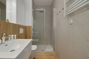 A modern bathroom with a glass-enclosed shower, a white sink, and a wooden vanity. - Cozy Apartment Near the Beach | Parking | Terrace (Międzywodzie)