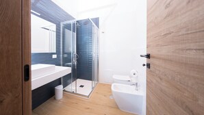 A modern bathroom with a glass shower enclosure, a white sink, and a bidet.