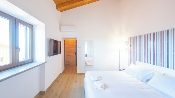 A hotel room with a wooden ceiling, a bed with white linens, a TV mounted on the wall, and a striped wall decoration.