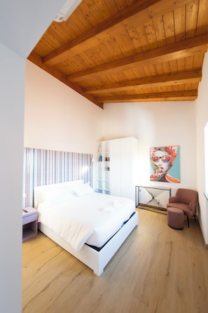 Ein Schlafzimmer mit Holzboden, einem Bett, einem Sessel, einem Nachttisch und einem an der Wand befestigten Regal.