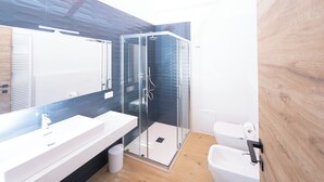 A modern bathroom with a glass-enclosed shower, a white sink, and a toilet.