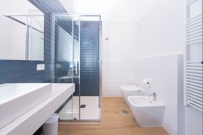 Un bany modern amb una cabina de dutxa de vidre, un lavabo blanc i un vàter.