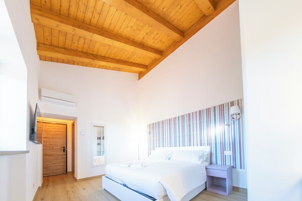 Ein Schlafzimmer mit Holzboden, einem Bett, einem Nachttisch, einem an der Wand befestigten Fernseher und einem Streifenmuster-Vorhang.