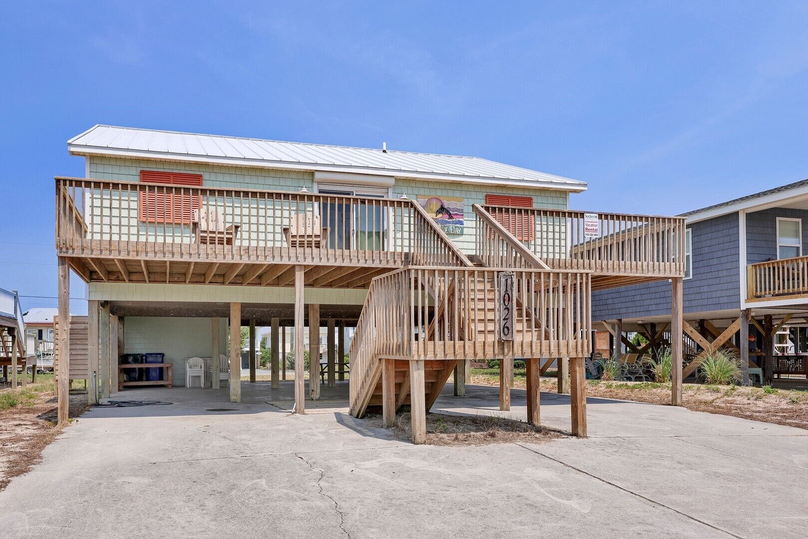 Une maison à deux étages avec un garage fermé, une terrasse en bois et un escalier menant à l’étage supérieur.