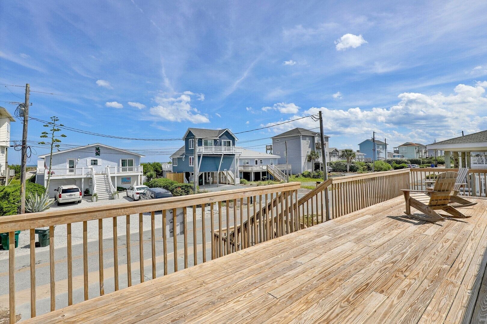 A wooden deck with a railing, a chair, and a view of houses and a street.