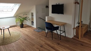 A room with a desk, chair, potted plant, and a TV mounted on the wall. - Quiet attic studio in Cologne-Holweide, a 2-minute walk to the S-Bahn station for Deutz/Messe (Köln)