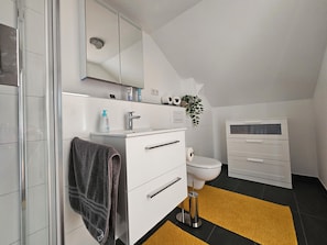 A modern bathroom with a glass shower enclosure, a white sink with a mirror above, a toilet, and a white cabinet with drawers.