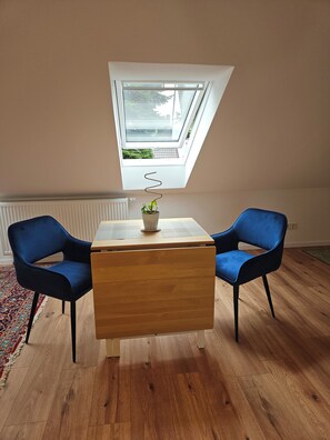 A room with a skylight, a wooden table, two blue chairs, and a potted plant.