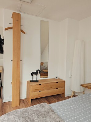 A bedroom with a wooden dresser, a mirror, a bedside table, a rug, and a wooden chair.