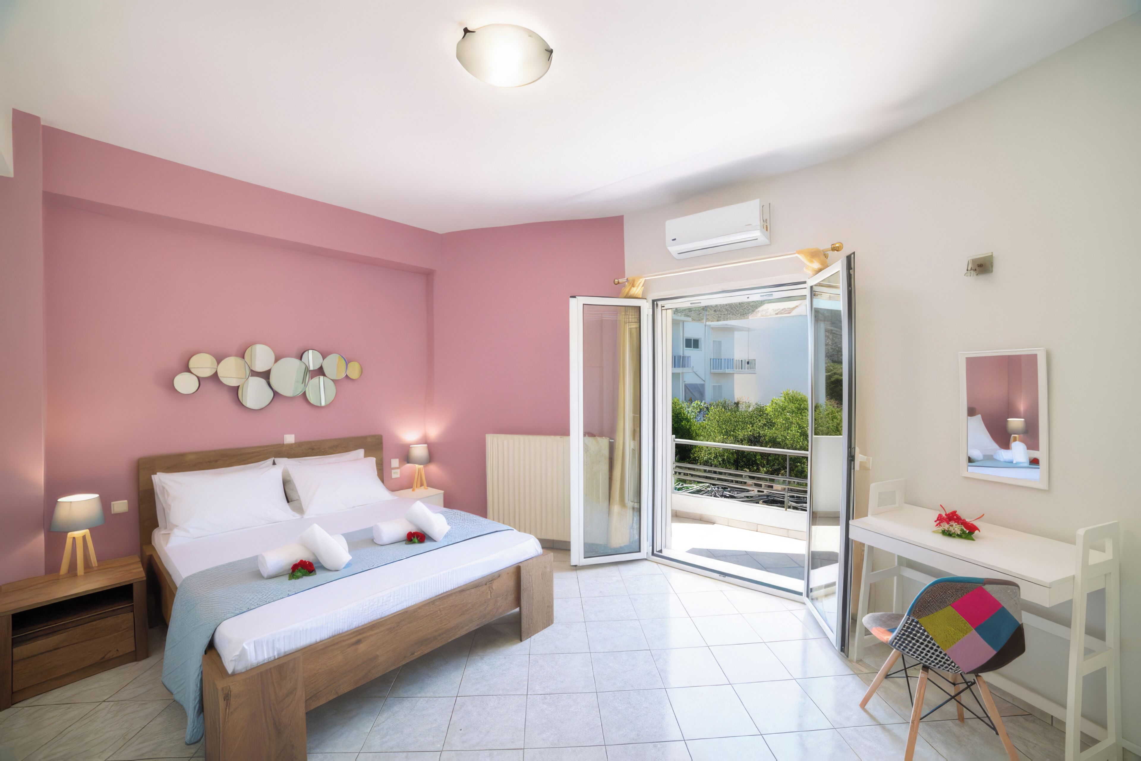 Un dormitorio con cama, mesitas de noche, escritorio, silla, balcón y vistas a zonas verdes.