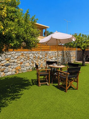 An outdoor seating area with a stone wall, a table with chairs, and an umbrella. - Villa Morea With Pool Near Chania City (Chania)