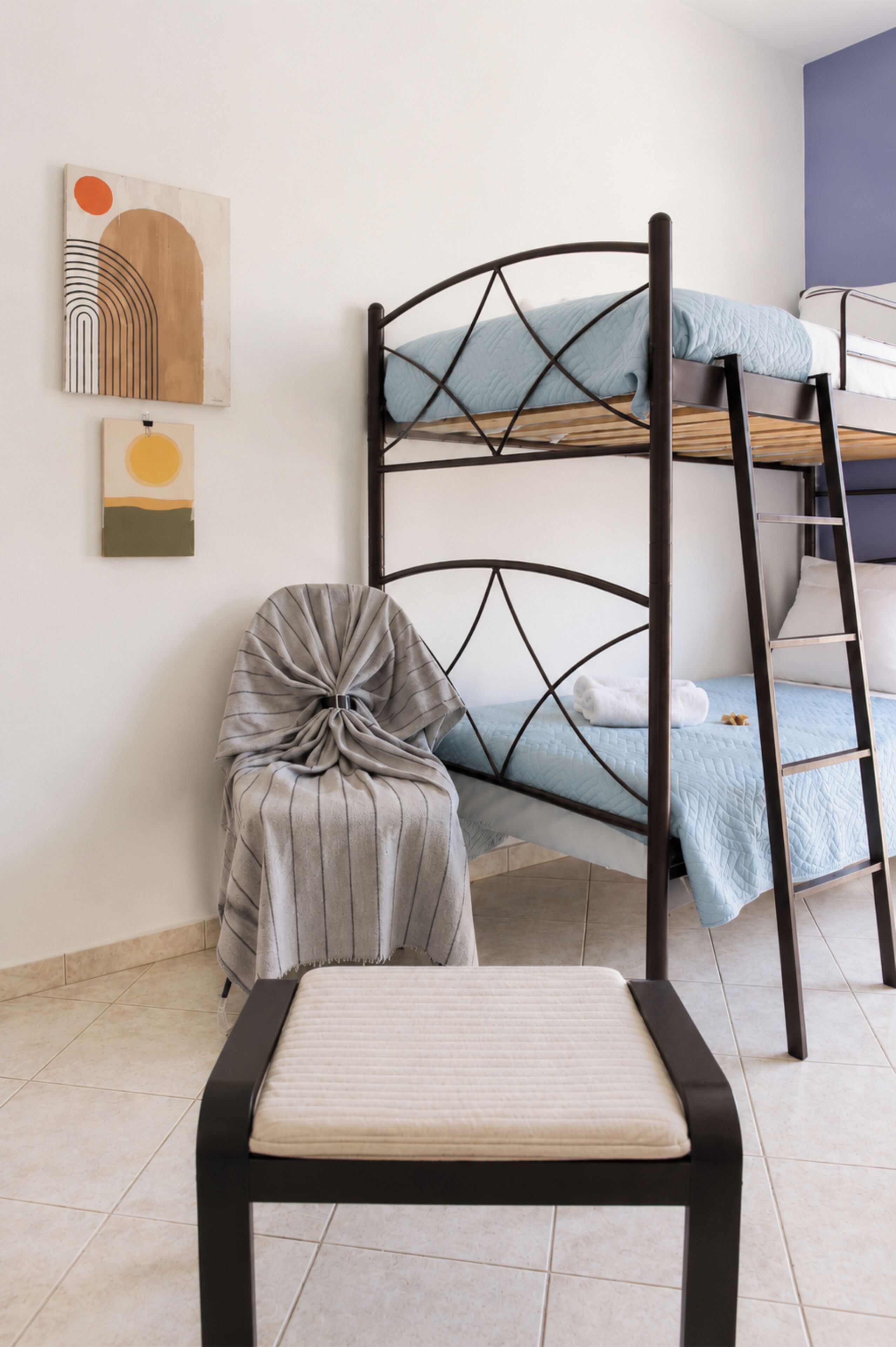 Un lit superposé avec une échelle, un fauteuil rembourré et des œuvres d’art accrochées au mur.
