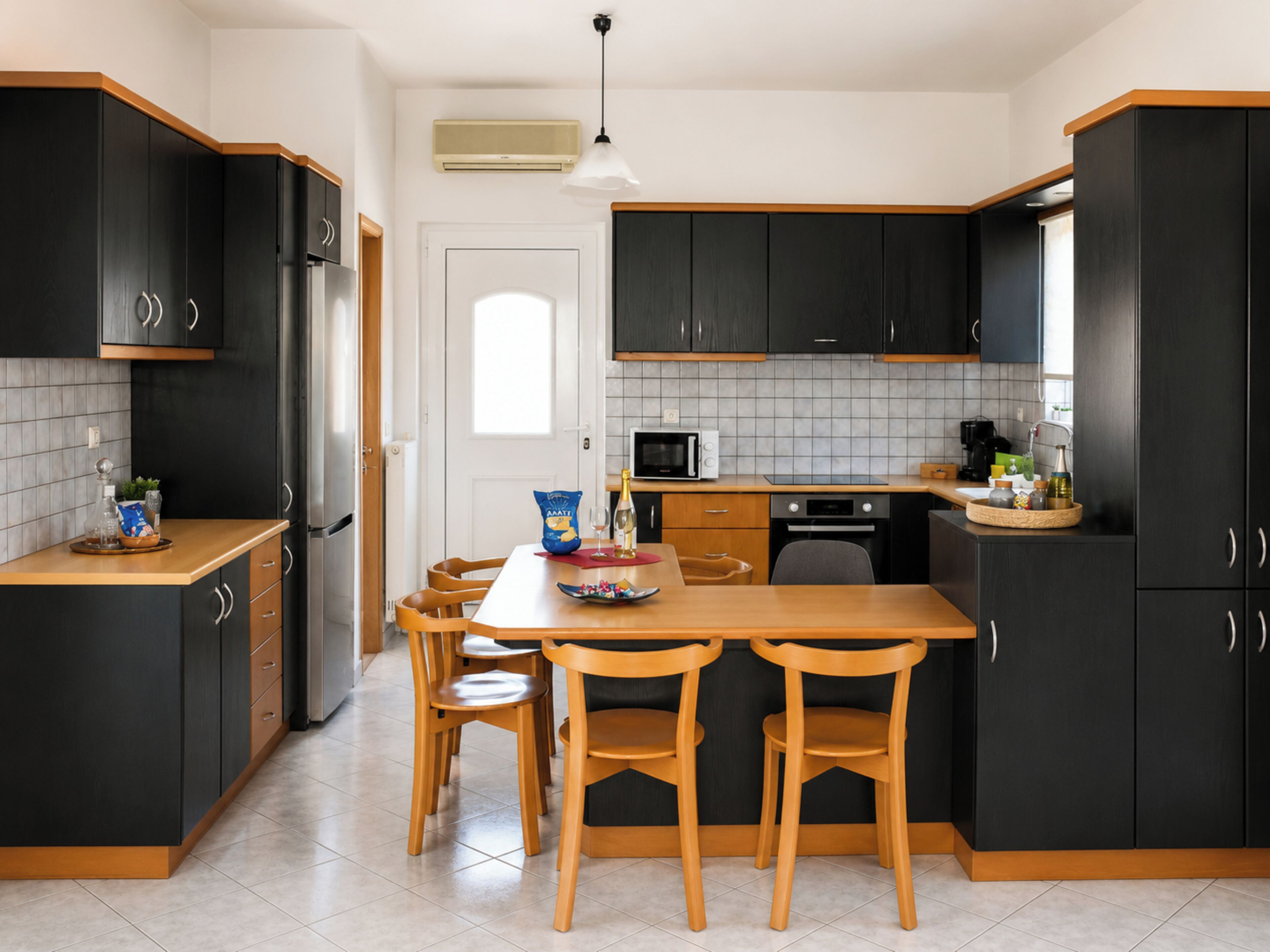 A modern kitchen with dark cabinetry, a wooden dining table, and chairs.
