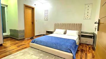 Quarto com cama, mesa de cabeceira, ventilador de teto e piso de madeira.