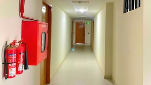 A hallway with an EXIT sign, fire extinguishers, and a ceiling vent.