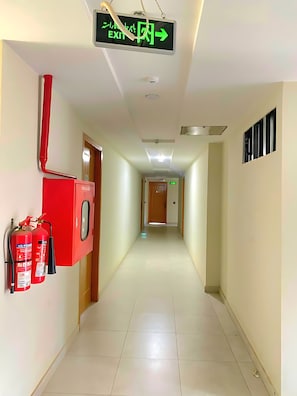 A hallway with an EXIT sign, fire extinguishers, and a ceiling vent. - AAA Guest House (Bahria Town)