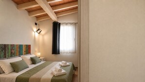 Een slaapkamer met een bed, kussens, een nachtkastje, een wandlamp en een raam met gordijnen.