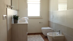 Een kleine, moderne badkamer met toilet, wastafel en een raam.