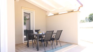 Een overdekt terras met een tafel en stoelen, een deur naar een binnenruimte en een houten vloer.