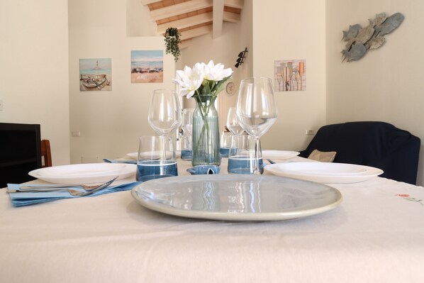 A dining table set with plates, glasses, and a vase of flowers. - Mar | House in Solanas between sea and nature (Cuili Murvoni)