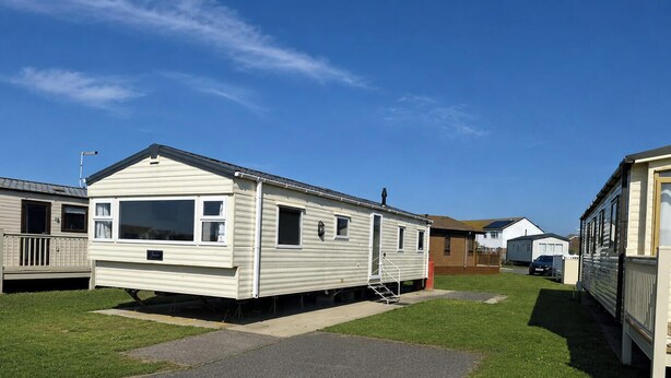 Ein Wohnmobil mit Veranda, einer kleinen angebauten Garage und blauem Himmel.