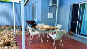A covered patio with a wooden deck, white wicker chairs, and a wooden table. - Karoo Nest Calitzdorp (Calitzdorp)